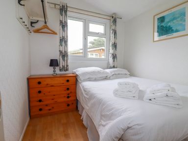 A bedroom with a double bed towels on the bed wooden chest of drawers and a window with curtains at Constantine Bay near St Merryn