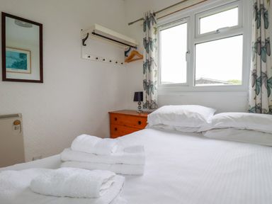 A bedroom with a bed and white towels on it next to a wooden chest of drawers and a window with floral curtains at Constantine Bay near St Merryn