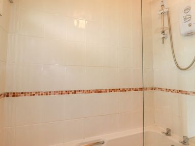 A bathroom with a bathtub shower and tiled walls at Constantine Bay near St Merryn