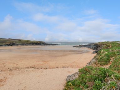 A sandy beach with rocky cliffs and grassy areas under a blue sky at Constantine Bay near St Merryn