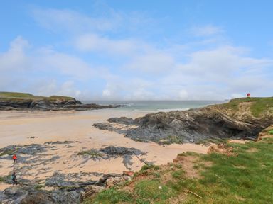 A sandy beach with rocky formations and grassy cliffs near the ocean at Constantine Bay near St Merryn