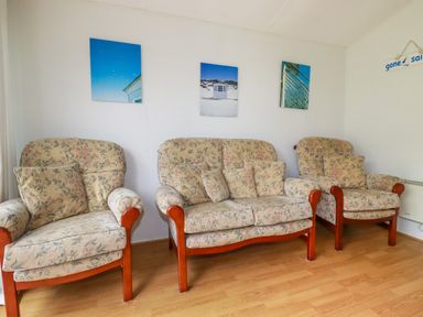 A living room with two armchairs and a two-seater sofa with floral upholstery and wooden legs at Porthcothan Bay in St Merryn
