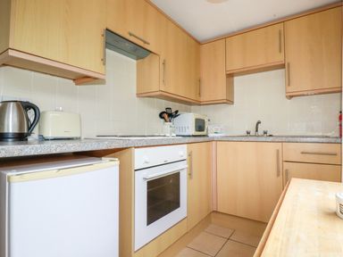 A kitchen with wooden cabinets a white oven a small refrigerator a kettle a toaster and a microwave at Porthcothan Bay in St Merryn