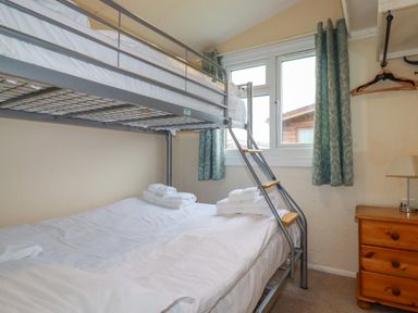 A bedroom with a metal bunk bed and a wooden dresser under a window with green curtains at Porthcothan Bay in St Merryn