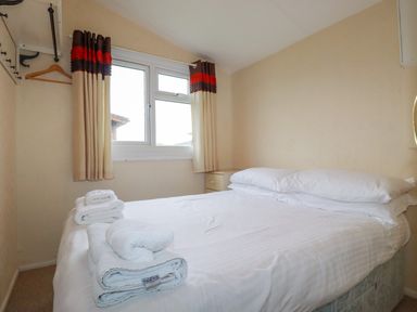 A bedroom with a double bed white bedding folded towels on bed window with curtains and a small bedside table at Porthcothan Bay in St Merryn