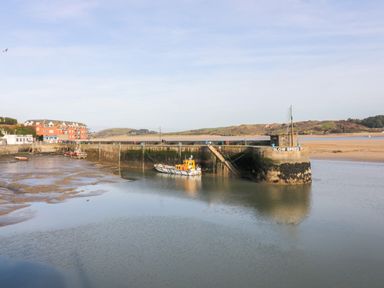 A small harbor with boats docked near a pier with a slow speed sign and buildings in the background at Porthcothan Bay in St Merryn