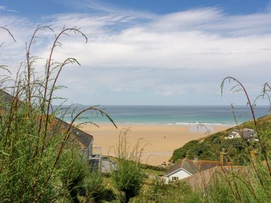 A coastal view with sand beach and ocean beyond houses and vegetation at Porthcothan Bay in St Merryn