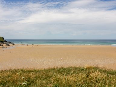 A beach with people walking on the sand and ocean in the background at Porthcothan Bay in St Merryn