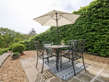 An outdoor patio with a table and four chairs under a large umbrella with plants and greenery at Holly Cottage in Llechwedd near Conwy