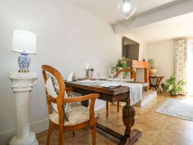 A dining area with a wooden table set with plates and glasses two wooden chairs and lamps at Holly Cottage in Llechwedd near Conwy