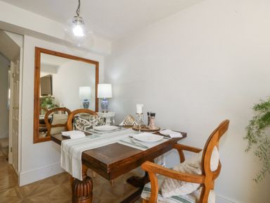 A dining table set for two with wooden chairs a large mirror on the wall and a lamp on a side table at Holly Cottage in Llechwedd near Conwy
