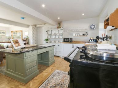 A kitchen with a green island, black stove, white cabinets, a plate rack and a microwave at Holly Cottage in Llechwedd near Conwy
