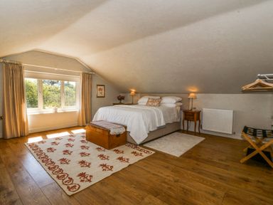 A bedroom with a bed side tables lamps wooden chest patterned rug window with curtains and wooden floor at Holly Cottage in Llechwedd near Conwy