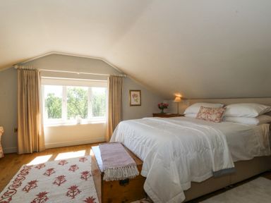 A bedroom with a bed a wooden chest a window with curtains and a side table with a lamp at Holly Cottage in Llechwedd near Conwy