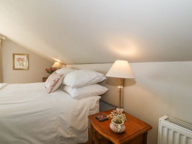 A bedroom with a bed pillows bedside tables lamps flowers and a radiator at Holly Cottage in Llechwedd near Conwy