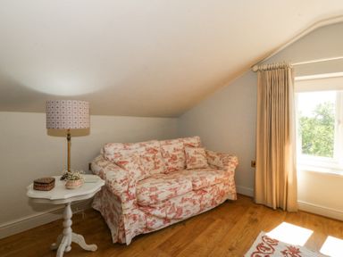 A small sitting area with a patterned sofa a white side table with a lamp and a window with curtains at Holly Cottage in Llechwedd near Conwy