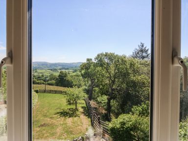 A countryside view of trees fields and hills through a window at Holly Cottage in Llechwedd near Conwy