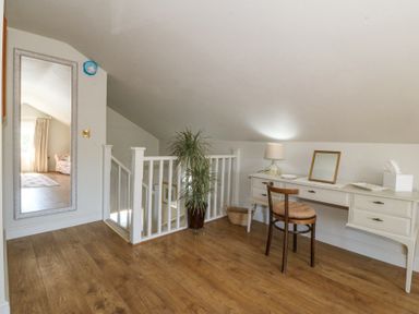 A small room with a wooden floor a white desk with a chair a table lamp a plant and a large wall mirror at Holly Cottage in Llechwedd near Conwy