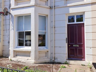 Exterior view of a building showing a window with a lamp inside and a maroon door at Flat 1 in Scarborough
