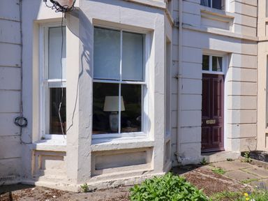 Exterior of a building showing a window with a lamp inside and a maroon door at Flat 1 Scarborough