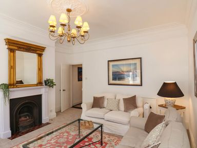 A living room with two sofas a glass coffee table a chandelier and a fireplace with a gold framed mirror at Flat 1 in Scarborough