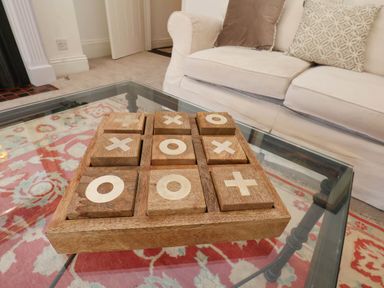 A wooden tic tac toe game on a glass coffee table with a patterned rug and a white sofa with cushions in the background at Flat 1 in Scarborough