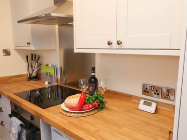 A kitchen countertop with a stove, knife set, cutting boards, bread, red peppers, basil, wine bottle, wine glasses, and cabinets at Flat 1 in Scarborough