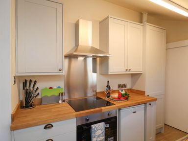 A kitchen with white cabinets a wooden countertop a stove an oven a knife set cutting boards and food items on the counter at Flat 1 in Scarborough
