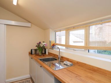 A kitchen area with a wooden countertop a sink a vase of flowers a toaster and window blinds at Flat 1 in Scarborough