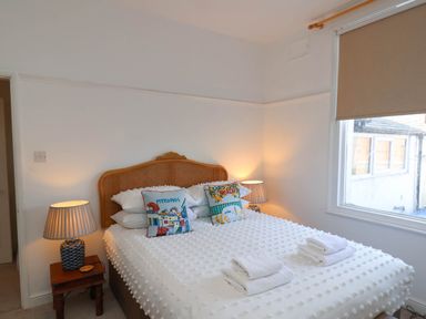 A bedroom with a double bed with white bedding and two pillows with travel themes two bedside tables each with a lamp and a window with a roller blind at Flat 1 in Scarborough