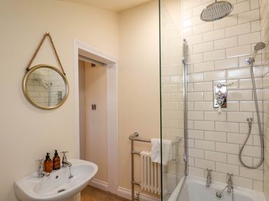 A bathroom with a sink and mirror and a bathtub with shower at Flat 1 in Scarborough