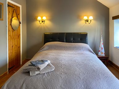 A bedroom with a bed covered with a patterned bedspread and folded towels on top at Lamorna Cottage in Chipping Norton
