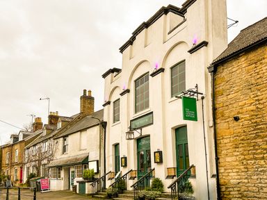 A street view of a theatre building with green signs and multiple doors surrounded by houses in Chipping Norton