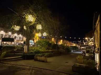 A street at night with decorative lights on a tree and along the road at Lamorna Cottage in Chipping Norton