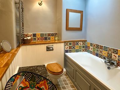 A bathroom with a bathtub a toilet a washbasin and decorative tiles at Lamorna Cottage in Chipping Norton