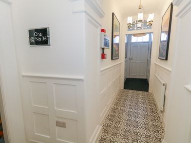 A hallway with patterned tile flooring white paneled walls a chandelier and framed artwork at Two @ No36 in Weymouth