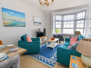 A living room with teal sofas a coffee table a television and large windows at Two @ No36 in Weymouth