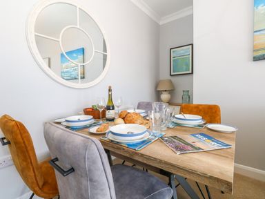 A dining table set with plates bowls glasses bread and wine in a room with chairs a lamp and round wall mirror at Two @ No36 in Weymouth
