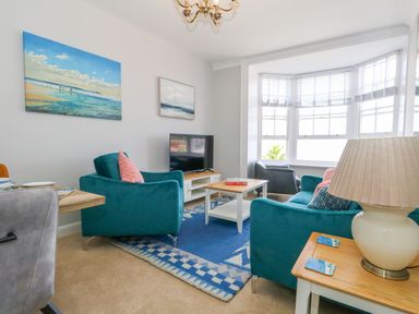 A living room with blue armchairs a coffee table a television and paintings on the wall at Two @ No36 in Weymouth