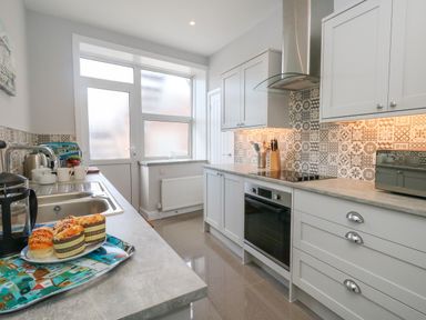 A kitchen with grey cabinets a tiled backsplash oven and a sink with food on a tray at Two @ No36 in Weymouth