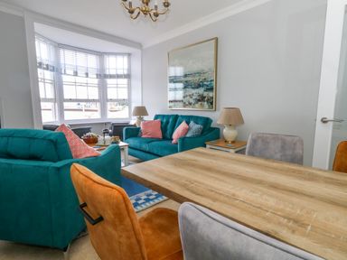 A living room with two teal sofas and a wooden dining table with chairs at Two @ No36 in Weymouth