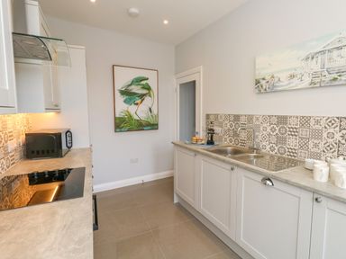 A kitchen with a cooktop microwave double sink and bird and beach paintings on the walls at Two @ No36 Weymouth