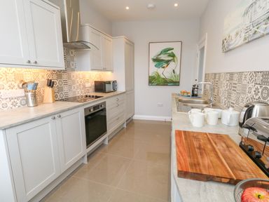 A kitchen with white cabinets a wooden cutting board a toaster a kettle mugs a microwave and wall art at Two @ No36 in Weymouth
