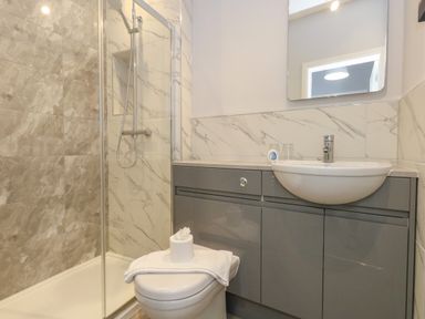 A bathroom with a shower, toilet, sink, and grey cabinets at Two @ No36 in Weymouth