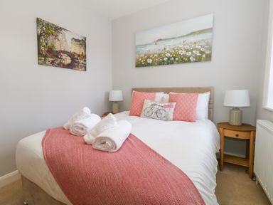A bedroom with a bed with white linens and pink pillows and two paintings on walls at Two @ No36 in Weymouth