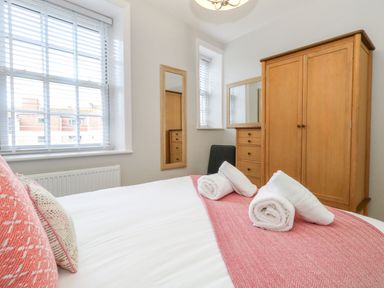 A bedroom with a bed with folded towels a wardrobe chest of drawers and windows with blinds at Two @ No36 in Weymouth