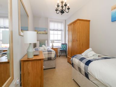 A bedroom with two single beds a wooden wardrobe a wooden chest of drawers with a lamp and a mirror on the wall at Two @ No36 in Weymouth