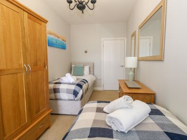 A bedroom with two single beds a wooden wardrobe a chest of drawers and a lamp at Two @ No36 Weymouth