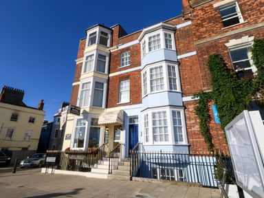 A brick building with blue and white accents and signs for Bay View Hotel on a street in Weymouth