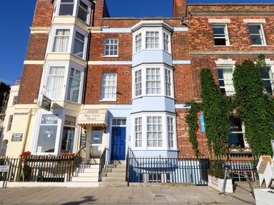 Exterior of a brick building with bay windows and signs for Bay View Hotel and Victoria Malaga at Two @ No36 in Weymouth